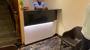 A reception desk with a person behind it, a plant, and a chair to the right. - Fabexpress Ashirwad Residency Arn To Gst (Mumbai)