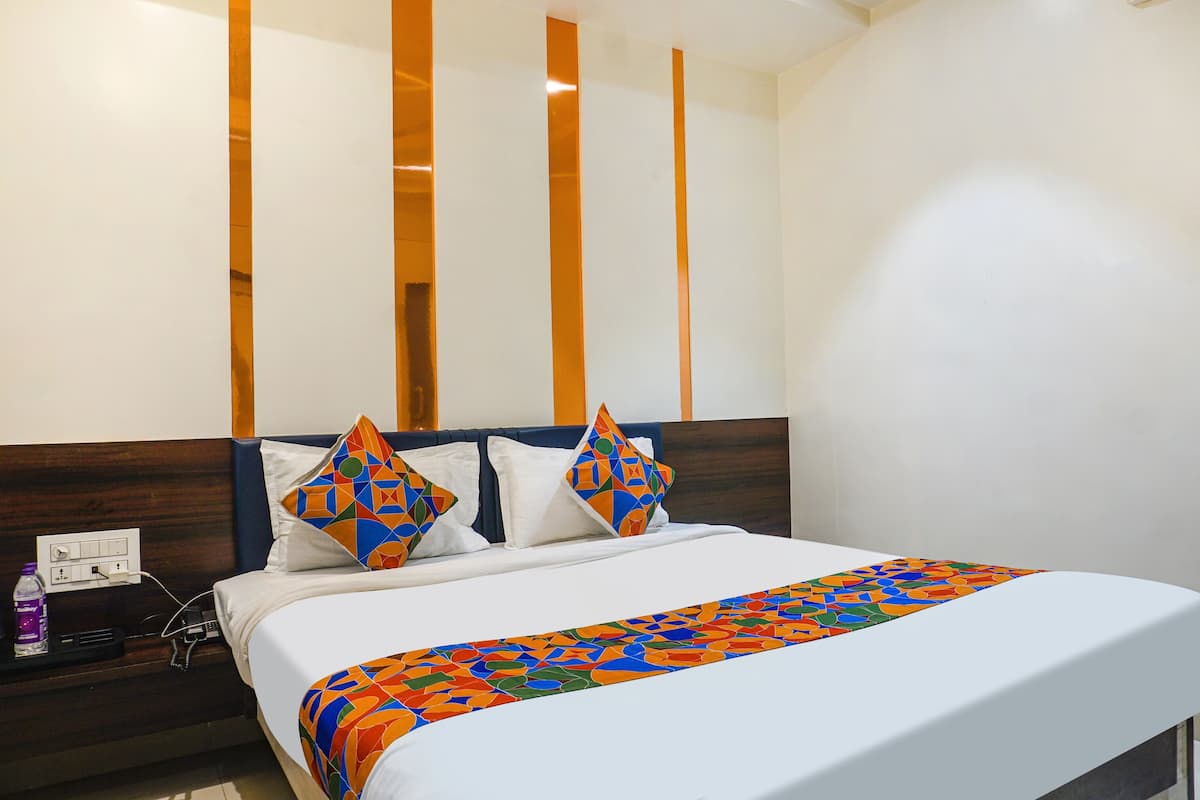 Cama bem arrumada com um manta colorida de padrão geométrico, cabeceira de madeira e parede branca com painéis de madeira verticais.