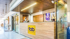 A hotel reception area with a wooden reception desk, a glass door, and a sign reading "fab hotels". - Fabhotel Tulsi Park (Rahata)