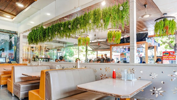 A restaurant interior with booths, tables, hanging plants, and a counter with people. - Fabhotel Tulsi Park (Rahata)