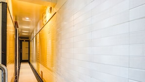 A corridor with white tiled walls and a yellow floor, leading to a door at the end. - Fabhotel Tulsi Park (Rahata)