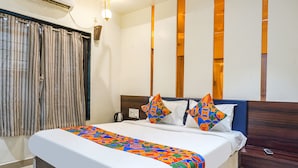 A neatly made bed with a colorful bedspread, a bedside table with a phone, and a wall-mounted air conditioner. - Fabhotel Tulsi Park (Rahata)