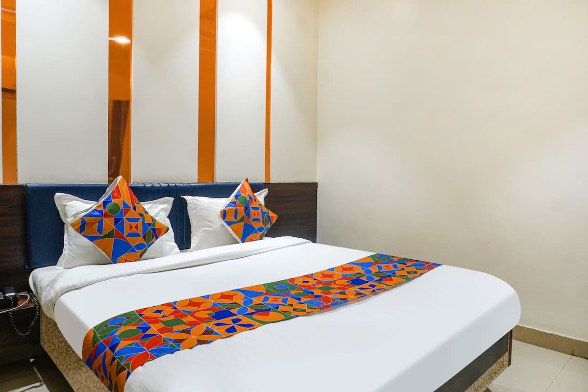 Cama bem arrumada com manta vibrante de padrão geométrico, roupa de cama branca e duas almofadas decorativas com desenho geométrico.