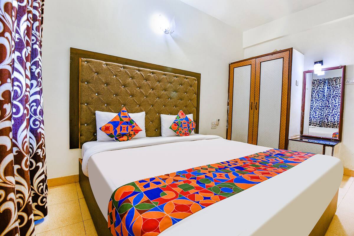 Une chambre d’hôtel avec un grand lit, une tête de lit capitonnée et une couvre-lit aux motifs géométriques et aux couleurs vives.