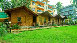 A row of wooden cabins with balconies, surrounded by a well-maintained lawn and tropical plants. - Via Jesant Valley Resort - Nr. Candolim Beach (Candolim)