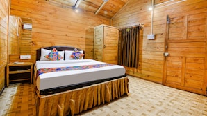 A wooden cabin bedroom with a bed, a nightstand, a wardrobe, and a window with curtains. - Via Jesant Valley Resort - Nr. Candolim Beach (Candolim)