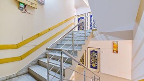 A staircase with marble steps and metal railings, leading to a landing with a framed artwork and a door with a decorative pattern. - Fabhotel Aayojan (Jaipur)