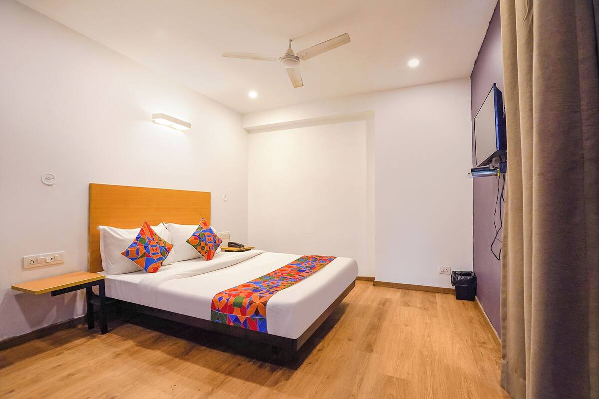 A hotel room with a bed, a bedside table, a ceiling fan, a TV mounted on the wall, and a wooden floor.