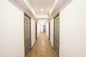 A long, narrow hallway with doors on both sides, a wooden floor, and a ceiling with recessed lighting. - Fabhotel Ramayana (Lucknow)