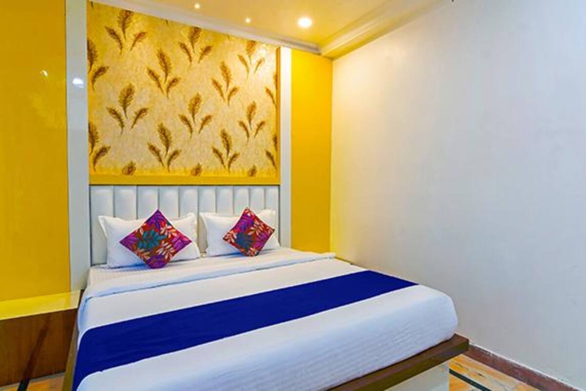 Une chambre d’hôtel avec un lit, deux oreillers, une tête de lit et un mur jaune orné d’un motif de feuilles.