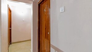 A hallway with a wooden door and a light switch on the wall. - Fabexpress Golden Palace (Kolkata)