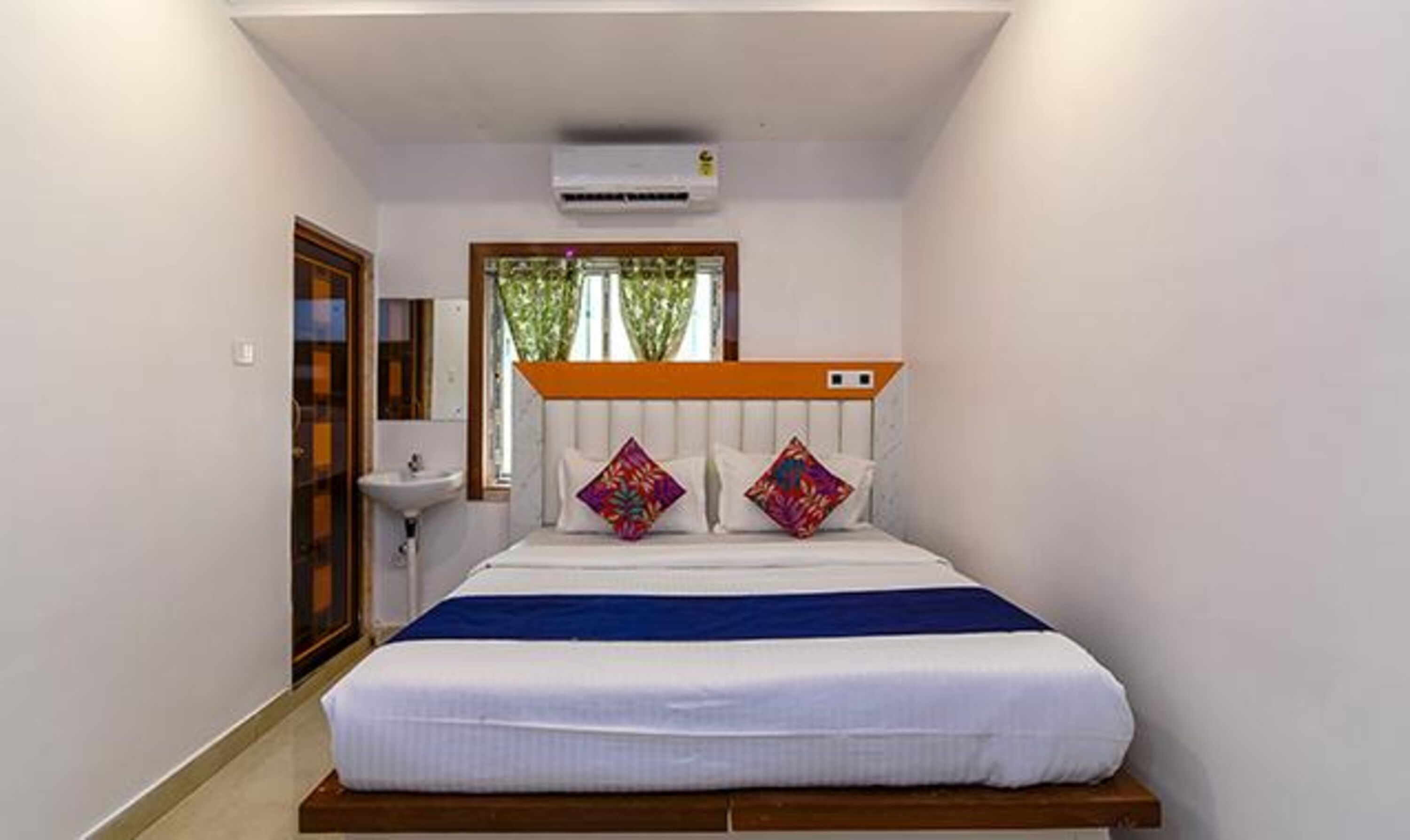 A bedroom with a bed, a window with a view, a bedside table, and a wall-mounted air conditioner.