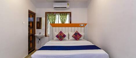 A bedroom with a bed, a window with a view, a bedside table, and a wall-mounted air conditioner.