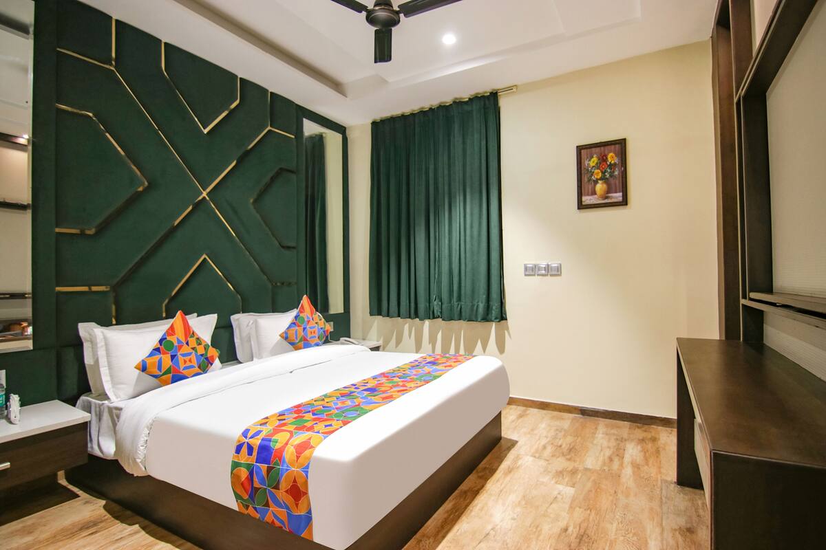 A hotel room with a bed, a nightstand, a desk, a ceiling fan, and a painting on the wall.