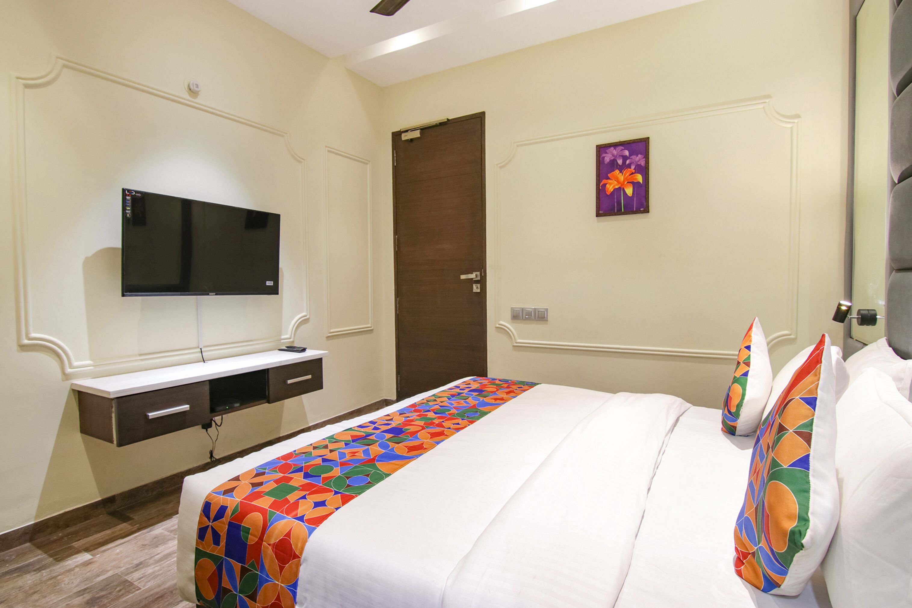 A hotel room with a bed, a TV mounted on the wall, a door, and a painting on the wall.