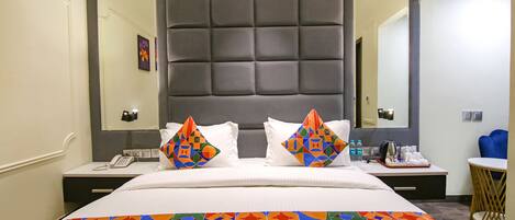 Una habitación de hotel con una cama grande, cabecera, mesita de noche con teléfono, mesita y una pequeña mesa redonda con una silla.