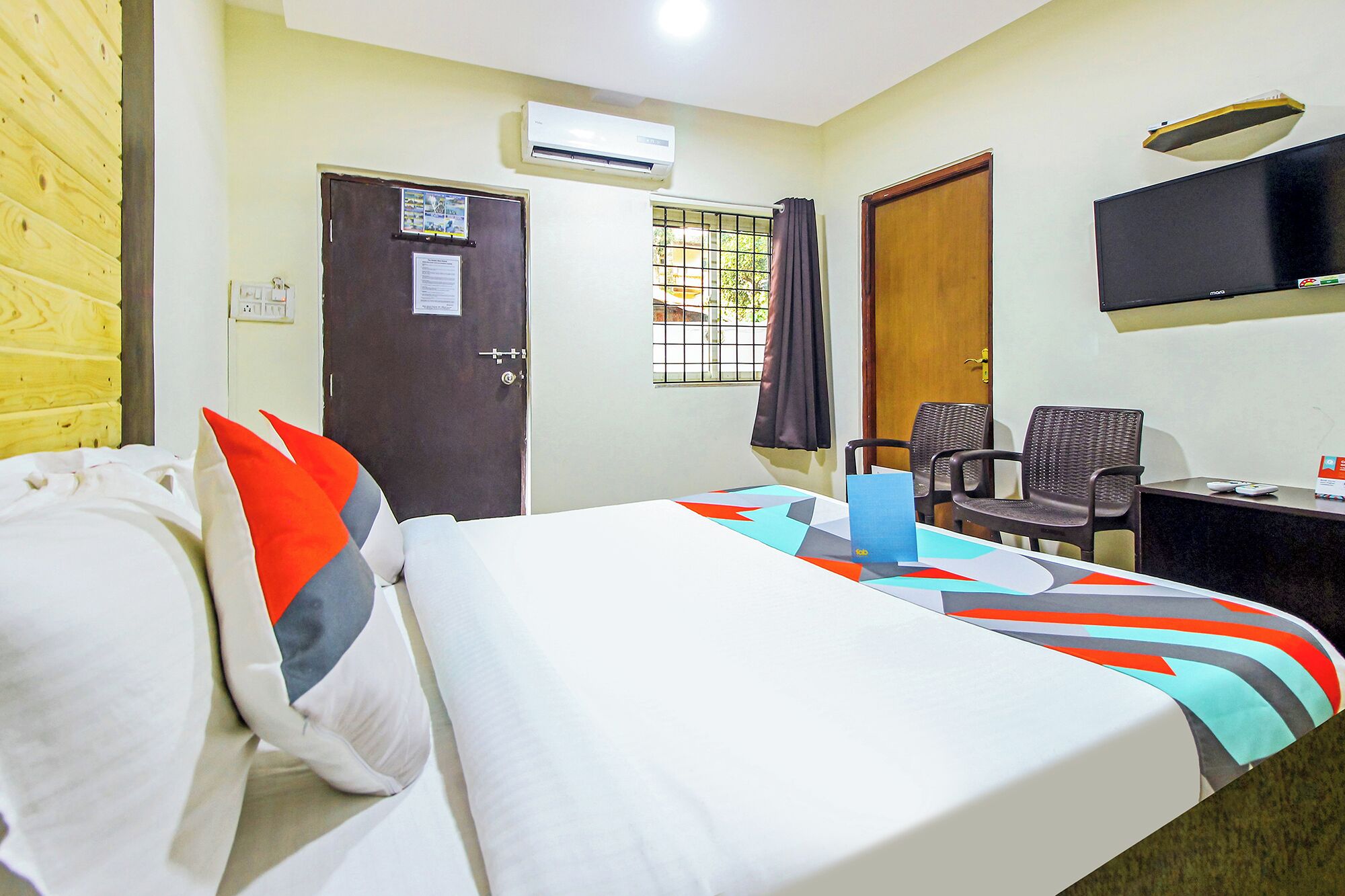 A hotel room with a bed, a desk, a chair, an air conditioning unit, and a television.