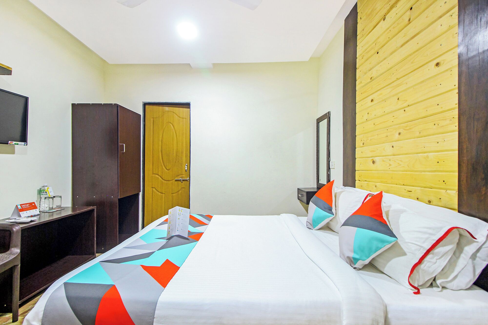 A hotel room with a bed, a desk, a chair, a TV, and a wooden wall panel.