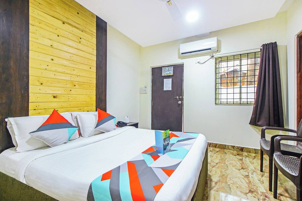 Ein Hotelzimmer mit Bett, Sessel, Klimaanlage, Tür und einem Vorhangfenster.