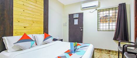 Ein Hotelzimmer mit Bett, Sessel, Klimaanlage, Tür und einem Vorhangfenster.