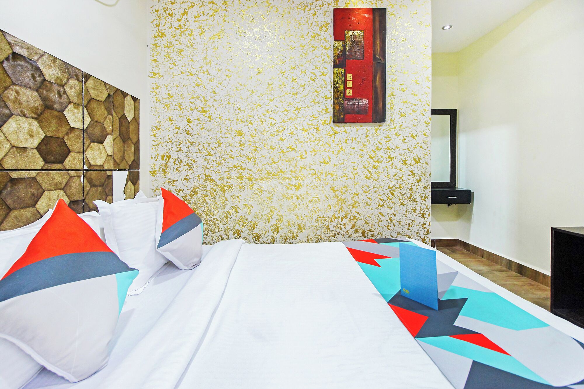 A hotel room with a bed, a stone-patterned wall, a mirror, and a small black side table.