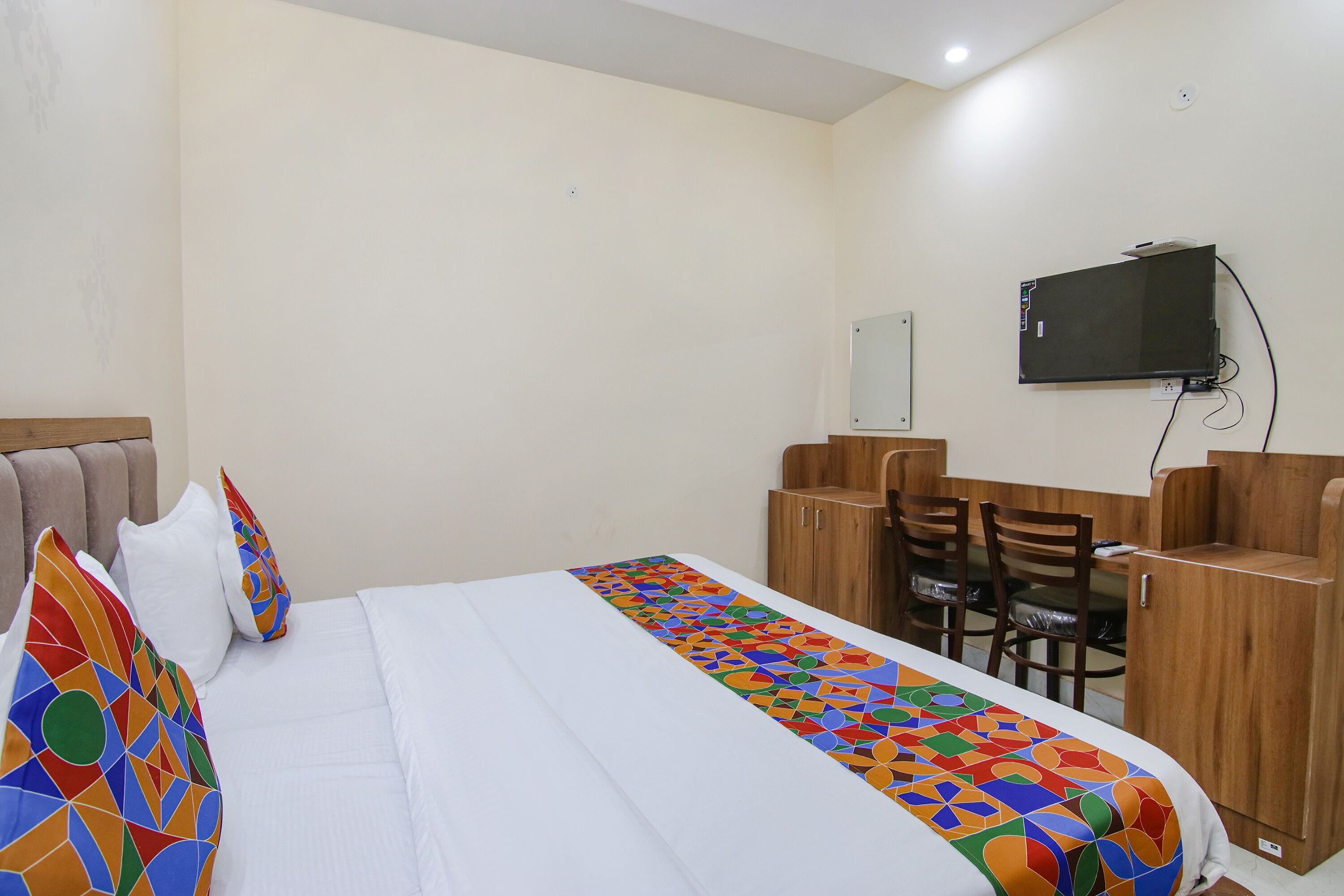 A hotel room with a bed, a desk, a chair, and a television mounted on the wall.