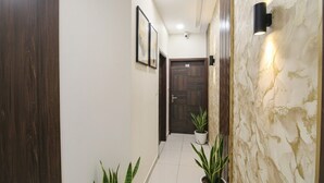 Un pasillo con puerta de madera, plantas en macetas, obras de arte enmarcadas y una lámpara fijada a la pared.