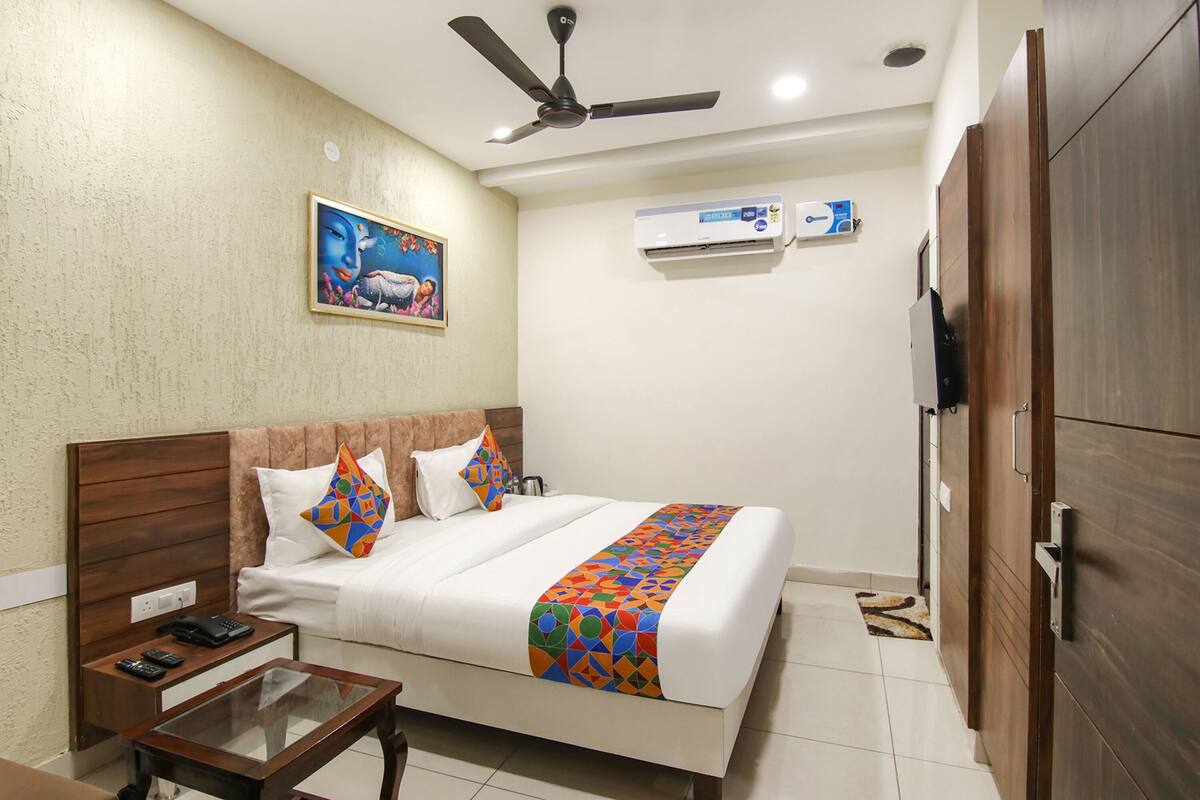 A hotel room with a bed, a bedside table with a phone and remote, a ceiling fan, an air conditioning unit, and a wardrobe.