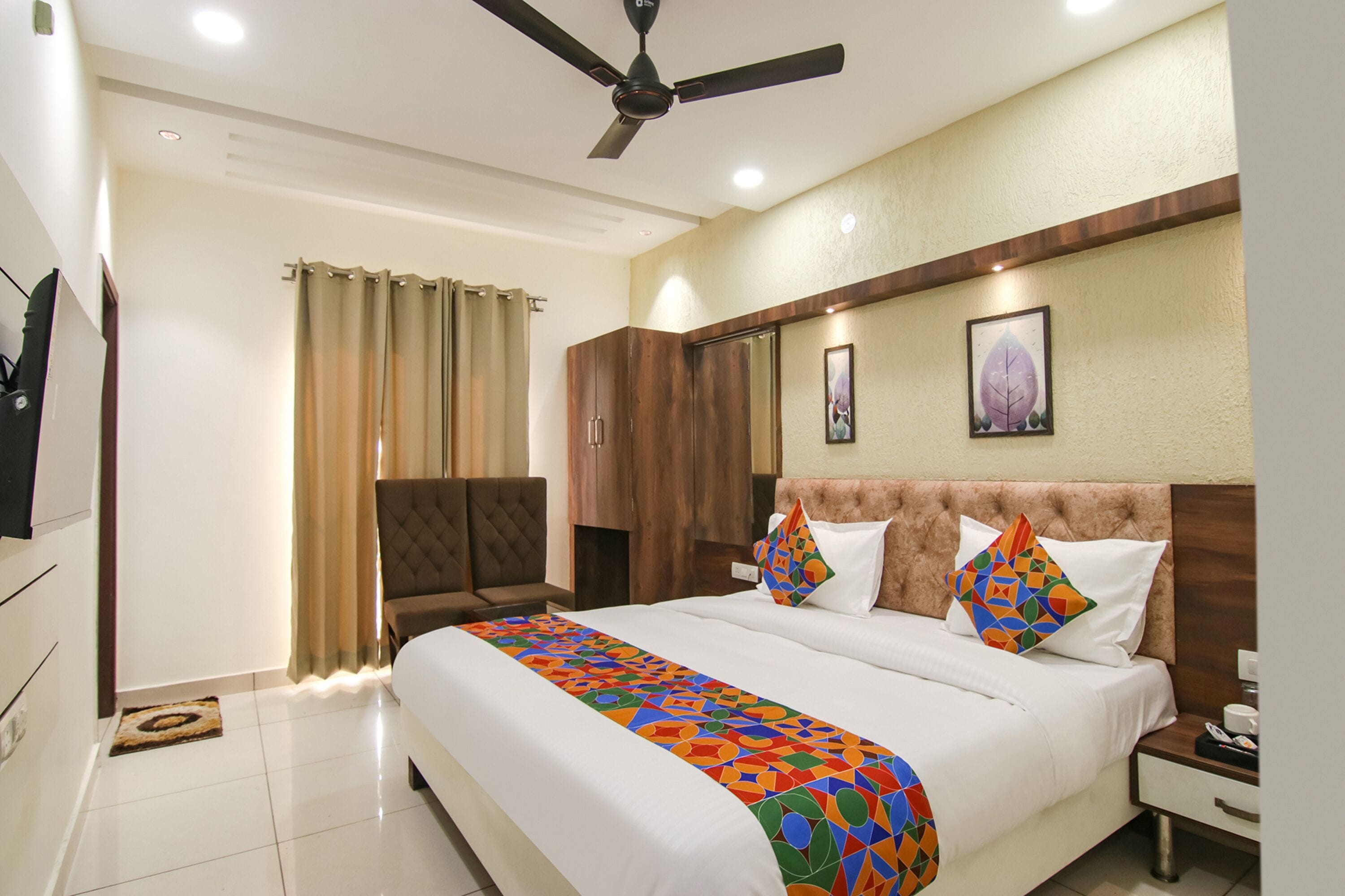 A hotel room with a bed, a nightstand, a chair, a ceiling fan, and a window with curtains.