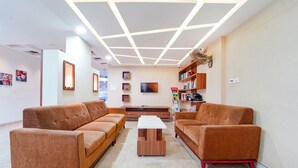 A modern living room with two brown sofas, a white coffee table, and a ceiling with geometric lighting. - FabHotel The South Gate (Thiruvananthapuram)