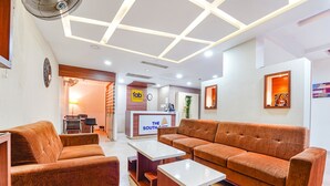 A modern hotel lobby with a sectional sofa, a reception desk, and a clock on the wall. - FabHotel The South Gate (Thiruvananthapuram)