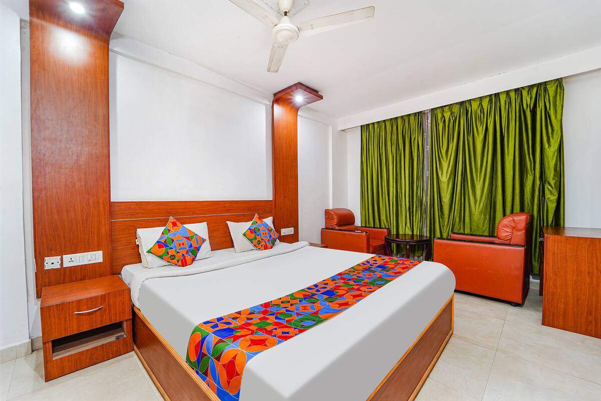 A hotel room with a large bed, wooden headboard, a desk, a chair, and a green curtain.