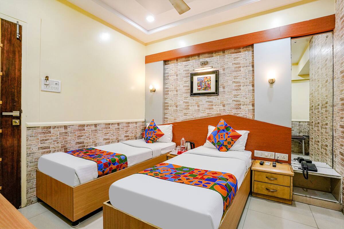 A hotel room with two beds, a wooden nightstand, a mirror, and a brick wall.