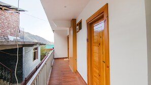 A corridor with a wooden door, a balcony with a metal railing, and a brick wall. - Fabhotel Ayana Inn (Dharamshala)