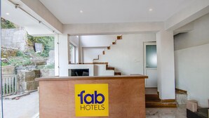 A hotel reception desk with a 'fab hotels' sign, a staircase, and a view of the outdoors. - Fabhotel Ayana Inn (Dharamshala)