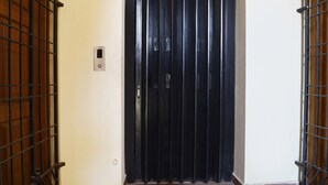 A black door with a metal gate, a wall-mounted intercom, and a small light switch. - Fabexpress Shree Shylee Niwas (Chennai)