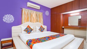 A bedroom with a bed, a nightstand, a wooden wardrobe, and a bathroom mirror. - Fabexpress Shree Shylee Niwas (Chennai)