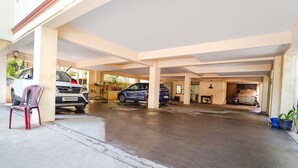 A covered parking area with two cars and a motorcycle, a bench, and potted plants. - Fabexpress Shree Shylee Niwas (Chennai)