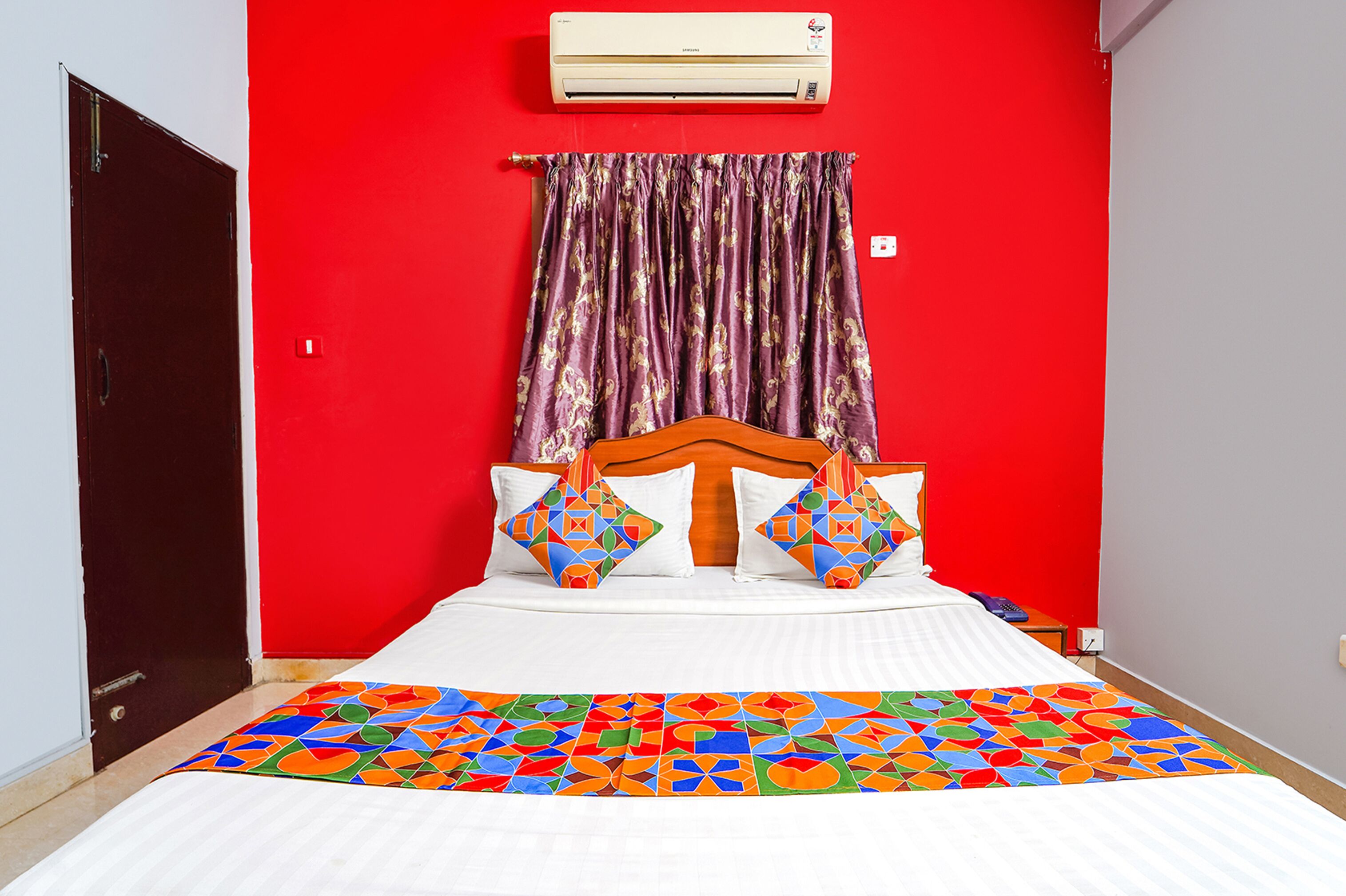 A room with a bed, red walls, a window with curtains, and an air conditioning unit.