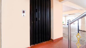 A hallway with a black door, a digital lock, and a metal handrail. - Fabexpress Shree Shylee Niwas (Chennai)