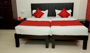 Una cama doble con cabecera negra, almohadas rojas, colcha blanca y manta roja.