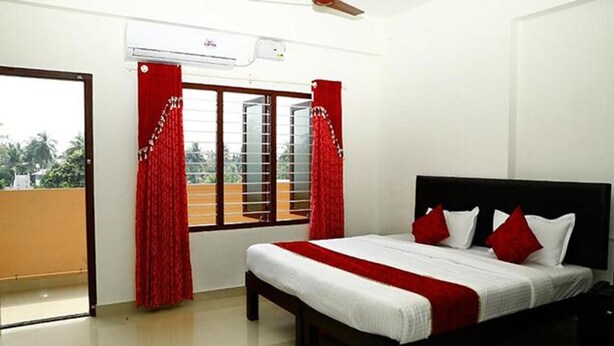 A bedroom with a bed, red curtains, and a window with a view. - Fabexpress Majestic Le Frank (Thiruvananthapuram)