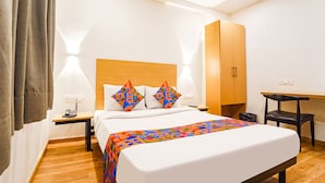 Une chambre d’hôtel comprenant un lit, une armoire en bois, un bureau, une chaise et une table de chevet avec une lampe.