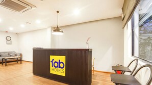 Un comptoir d’accueil avec une enseigne indiquant « fab hotels », un canapé, une table et des chaises dans une pièce lumineuse dotée d’une grande fenêtre.