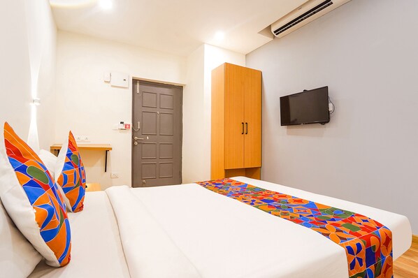 A hotel room with a bed, a TV mounted on the wall, a wooden wardrobe, and a door.