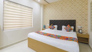 A bedroom with a large bed, a nightstand, a window with blinds, and a patterned wall.