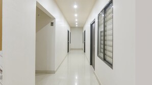 Corredor limpo e bem iluminado, com paredes brancas e piso brilhante, que dá acesso a várias portas e janelas.