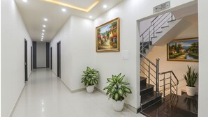A modern hotel corridor with a staircase, potted plants, and artwork on the walls.