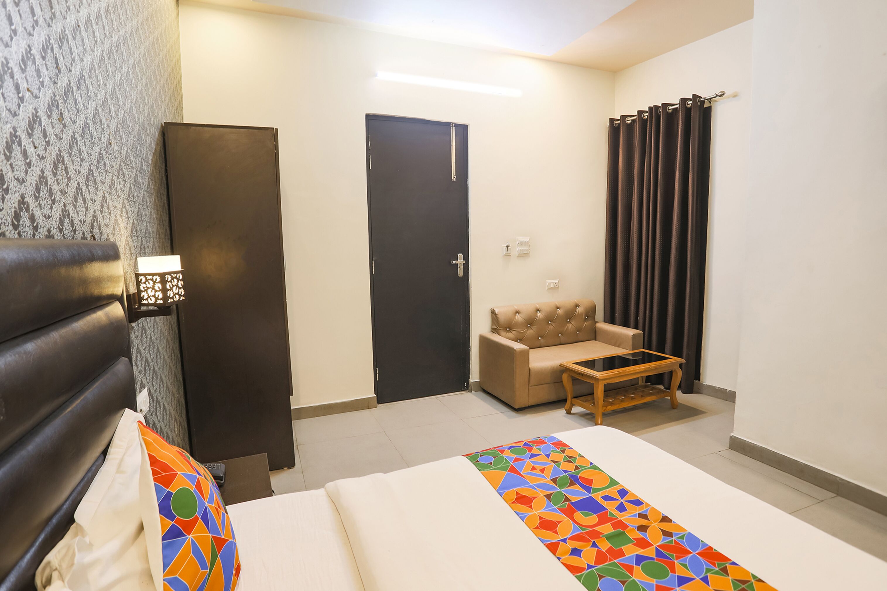 A hotel room with a bed, a sofa, a small table, a wardrobe, and a door.