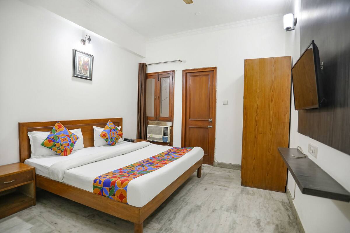A bedroom with a wooden bed, a nightstand, a wardrobe, and a TV mounted on the wall.